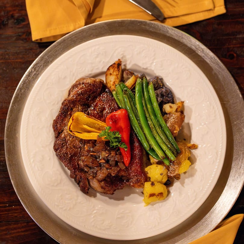Brazilian steak with sautéed onions, peppers, green beans, and roasted potatoes on a white plate.